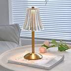 Brushed gold table lamp with clear ribbed crystal shade on a round base, lit.