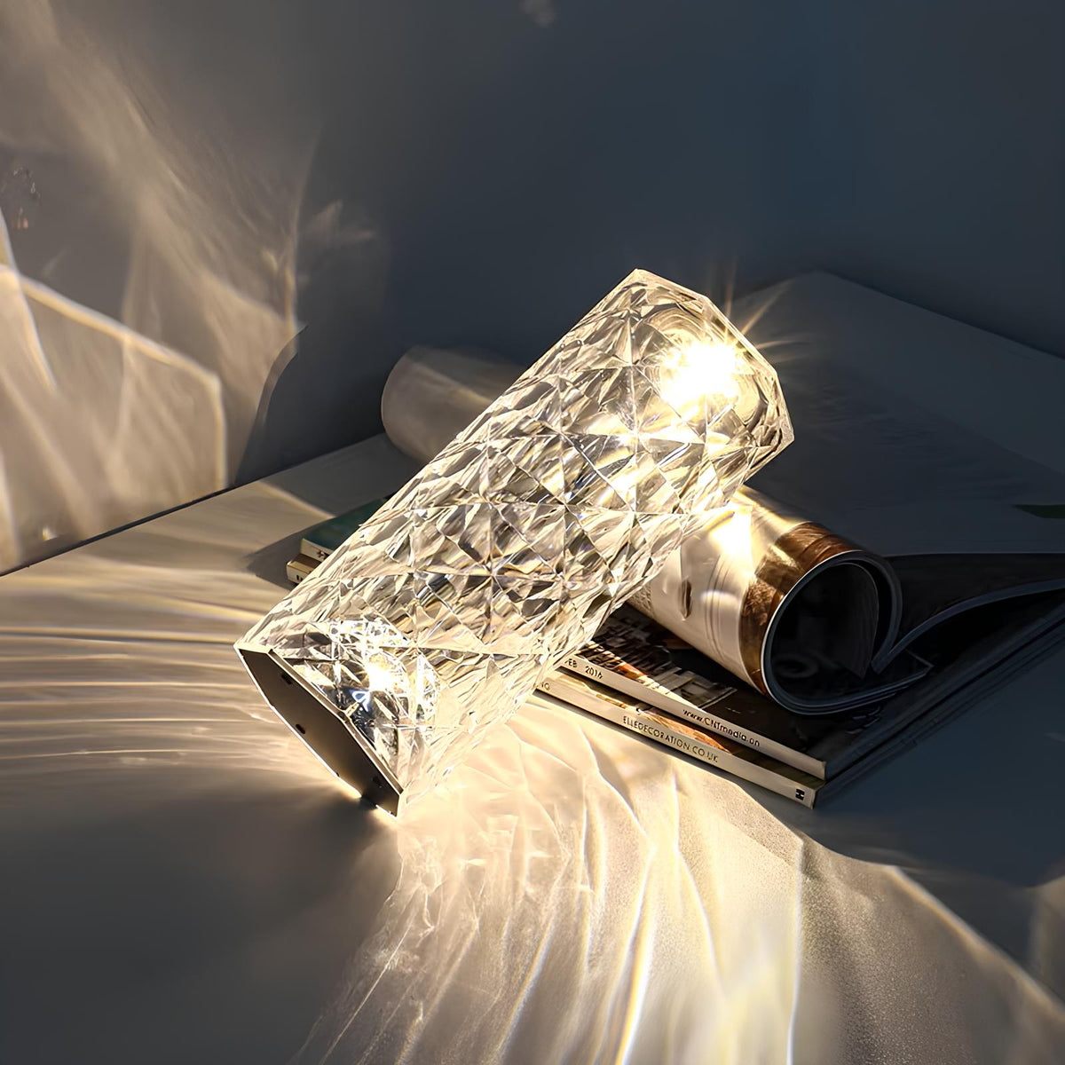 Faceted crystal table lamp with warm white light, cylindrical body on books.