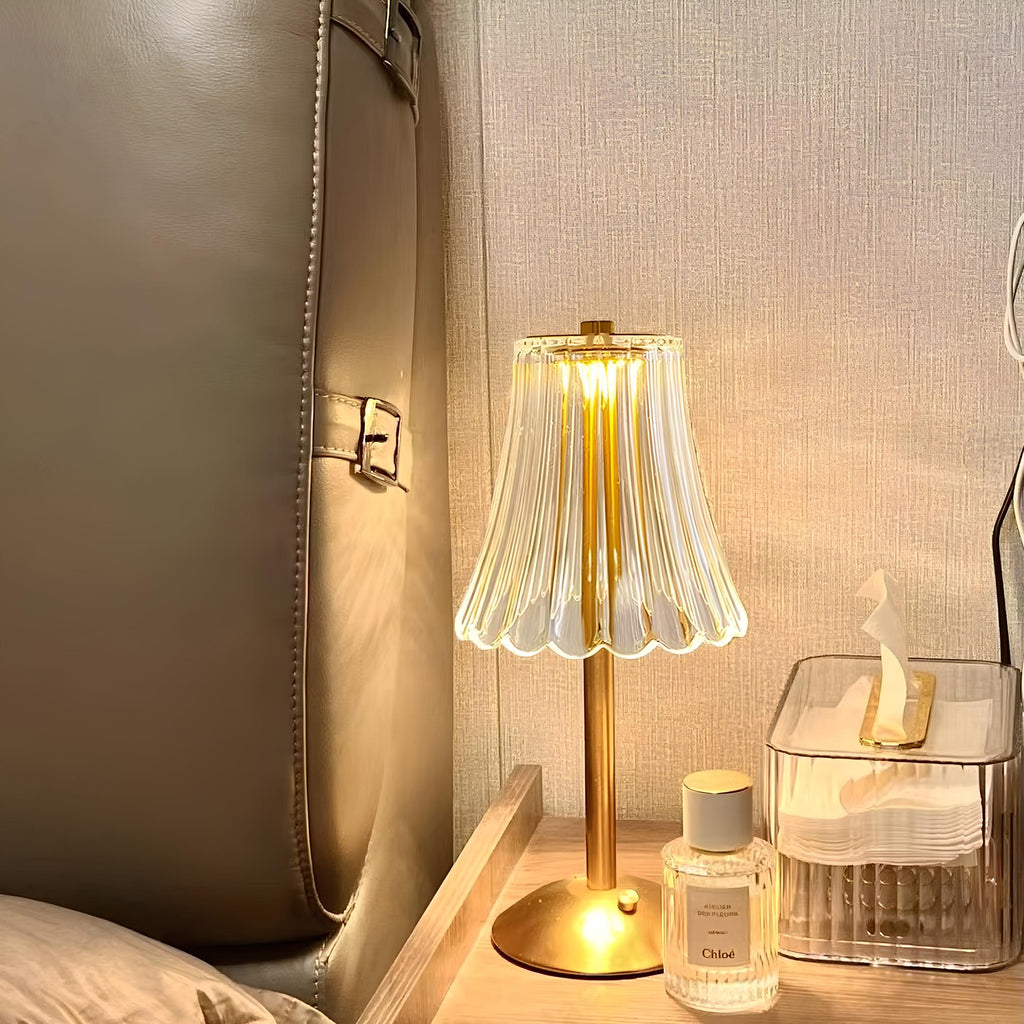 Gold table lamp with clear pleated crystal shade beside decor items, warm glow on.