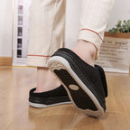 Black wide open-toe slippers with adjustable strap and grippy outsole, side view