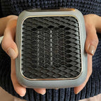 Portable electric heater held in hands, showing front grille and glowing coils