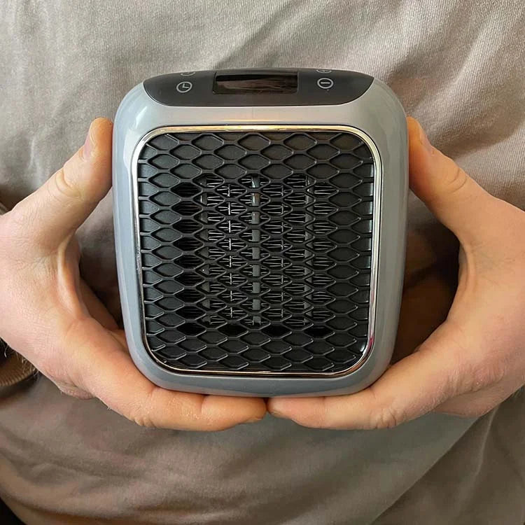 Compact electric fan heater held in hands with black honeycomb grille and top controls