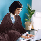 Burgundy flannel electric blanket draped over shoulders while typing on laptop