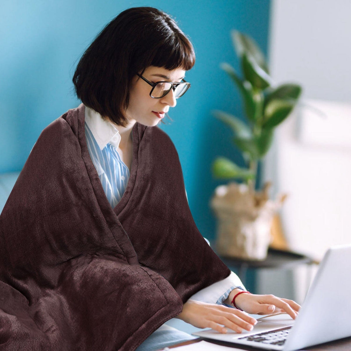 Burgundy flannel electric blanket draped over shoulders while typing on laptop
