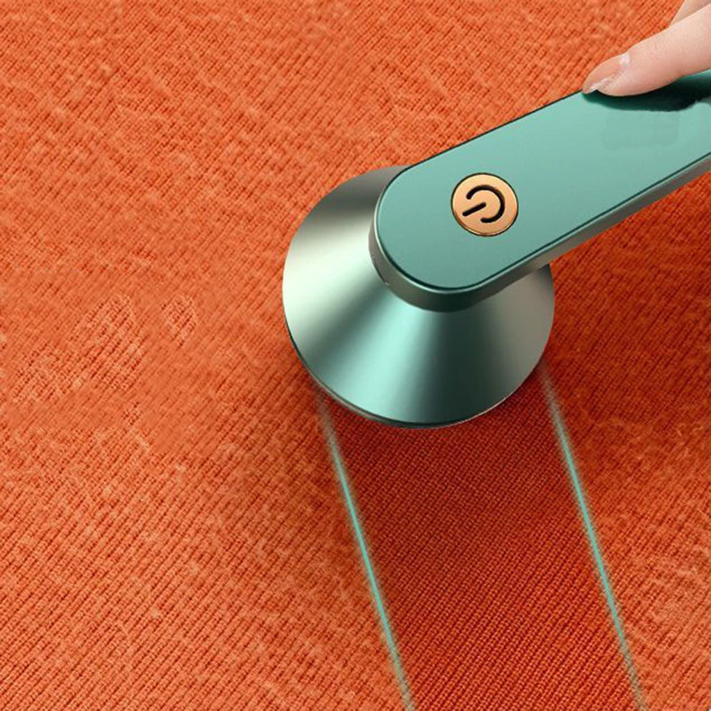 Green rechargeable fabric shaver over orange knit fabric with a hand pushing