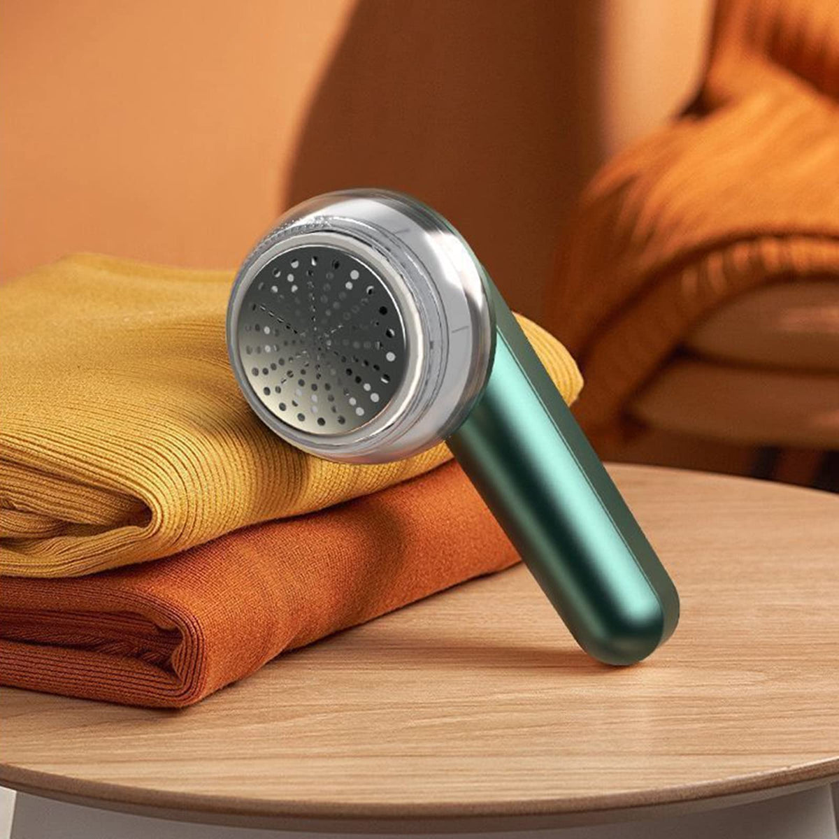 Teal rechargeable fabric shaver with perforated metal head on folded knit fabrics
