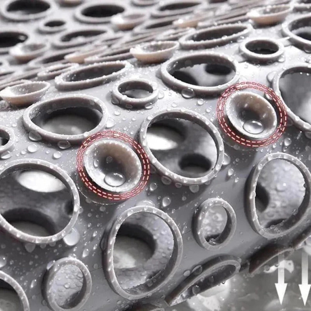 Close-up of gray shower mat drain holes with water droplets for grip