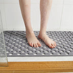 Gray shower mat with drainage holes under bare feet for non-slip grip.