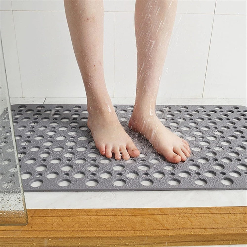 Gray shower mat with drainage holes under bare feet for non-slip grip.