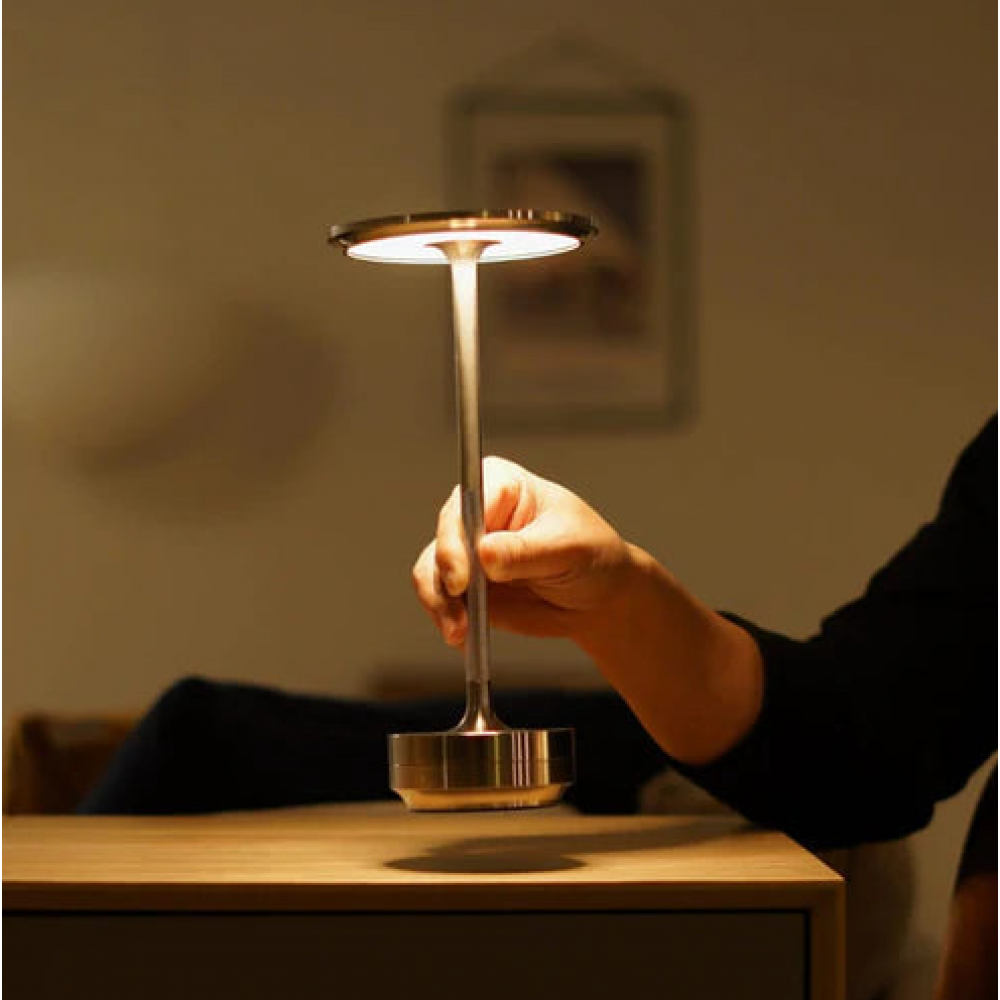 Hand touching cordless LED table lamp base with warm glowing round top shade