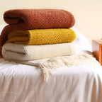 Folded knit throw blankets in brown, yellow, and white, each with fringe tassels