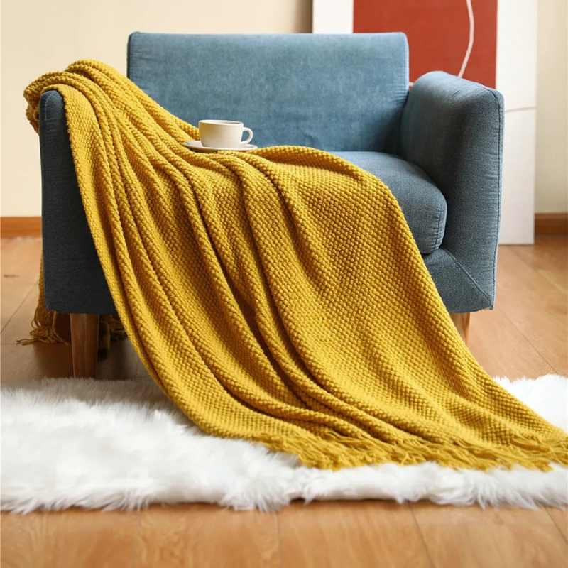 Mustard yellow knit throw blanket with fringe tassels, laid over a couch