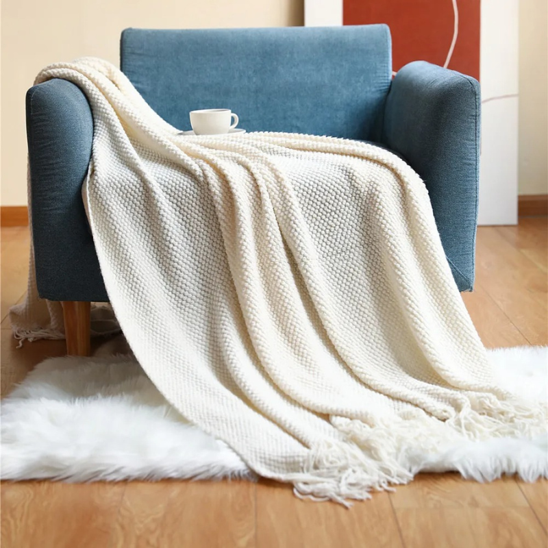 White knit throw blanket with fringe tassels, draped across a couch and floor