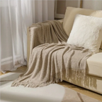 Beige knit throw blanket with fringe tassels, draped over a sofa cushion