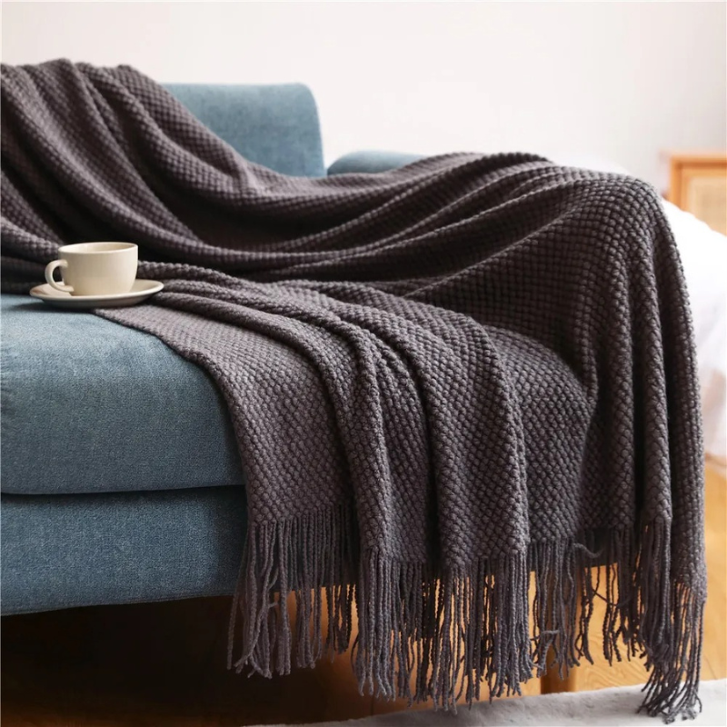 Dark charcoal knit throw blanket with tassels along the edge, textured acrylic look.