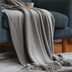 Light gray knit throw blanket with fringed ends and textured woven surface.