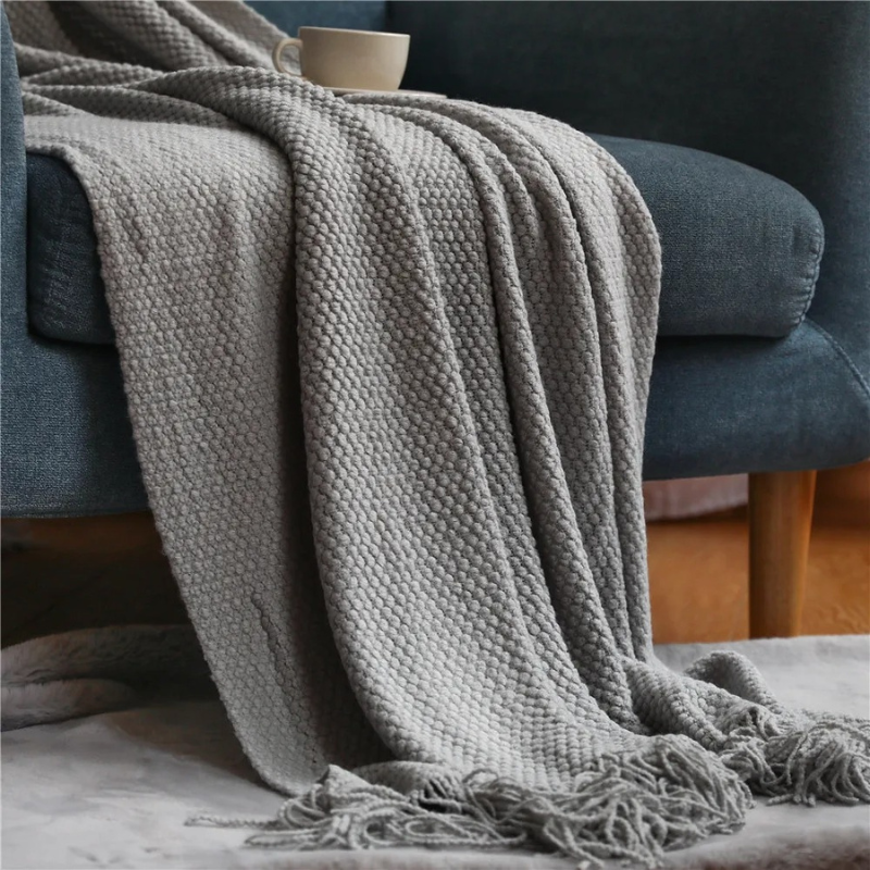 Light gray knit throw blanket with fringed ends and textured woven surface.