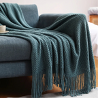 Teal knit throw blanket with chunky texture and long fringe tassels on a couch