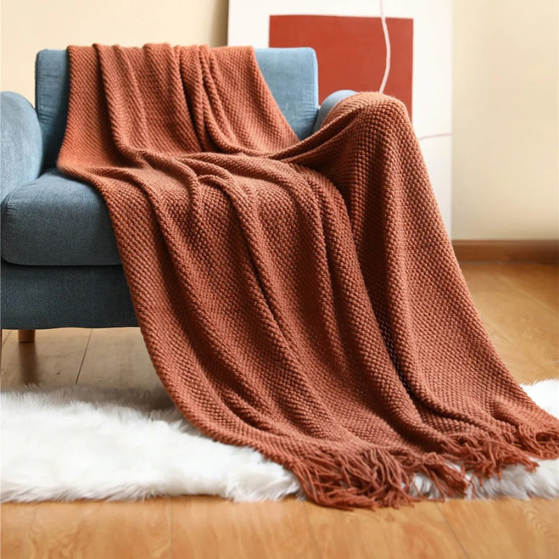 Rust orange knit throw blanket with fringe tassels, draped on a couch
