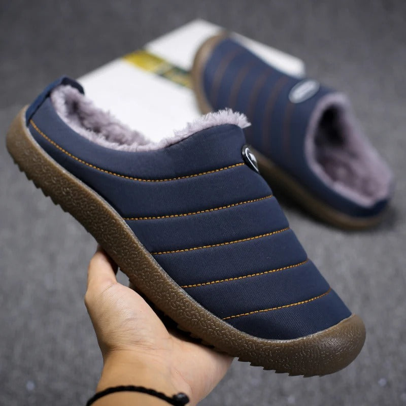 Men's lined slip-on slippers in blue, shown being held, with faux-fur interior and rubber sole