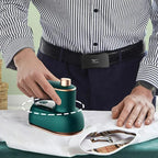 Green compact steam iron smoothing striped shirt fabric on a table