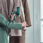 Green steam iron held above hanging garments with cord trailing